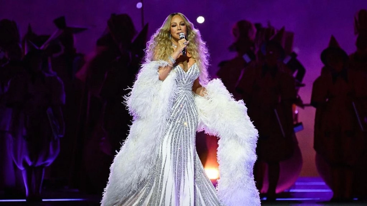 Mariah Carey performing at the 2026 Winter Olympics opening ceremony in Milan, with Andrea Bocelli and Sabrina Impacciatore on stage and a display of Italian flags and lights in the background.
