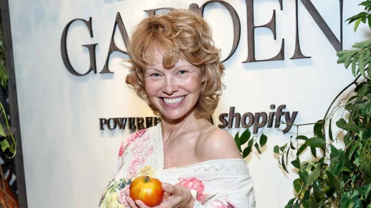 Pamela Anderson holding Sonsie Basic Balm in Sugar Dipped Rhubarb in a natural garden setting.