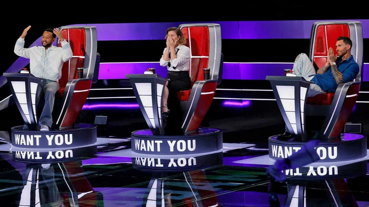 Kelly Clarkson, John Legend and Adam Levine seated in red chairs during The Voice Season 29 Blind Auditions.
