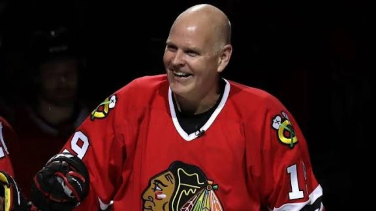 Troy Murray smiling in Blackhawks jersey on ice, holding hockey stick, during NHL career.