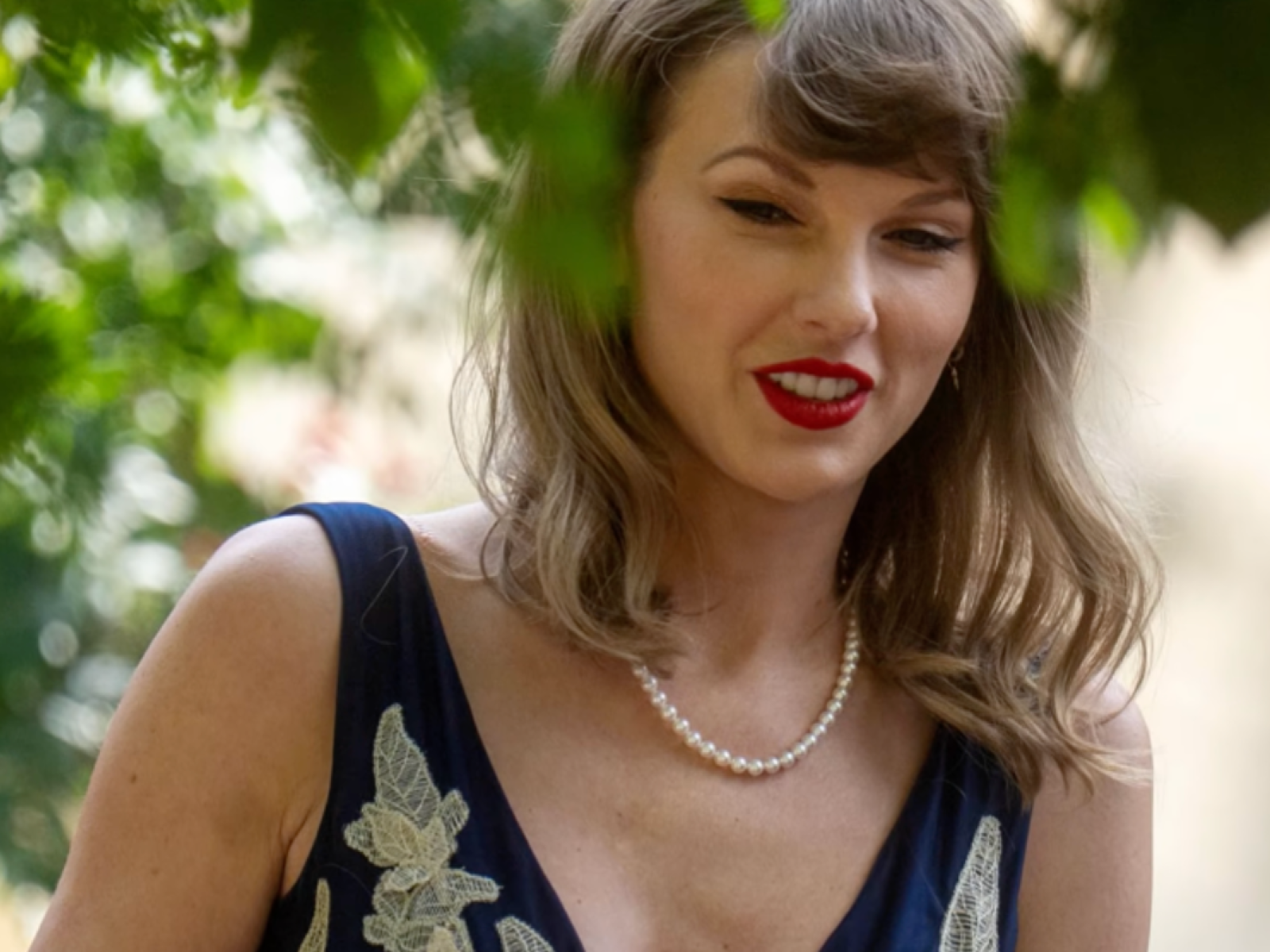 Taylor Swift at Oli Jacobs and Laura Sisk’s UK wedding on August 15, wearing a blue floral dress with shorter hair and her signature bangs.